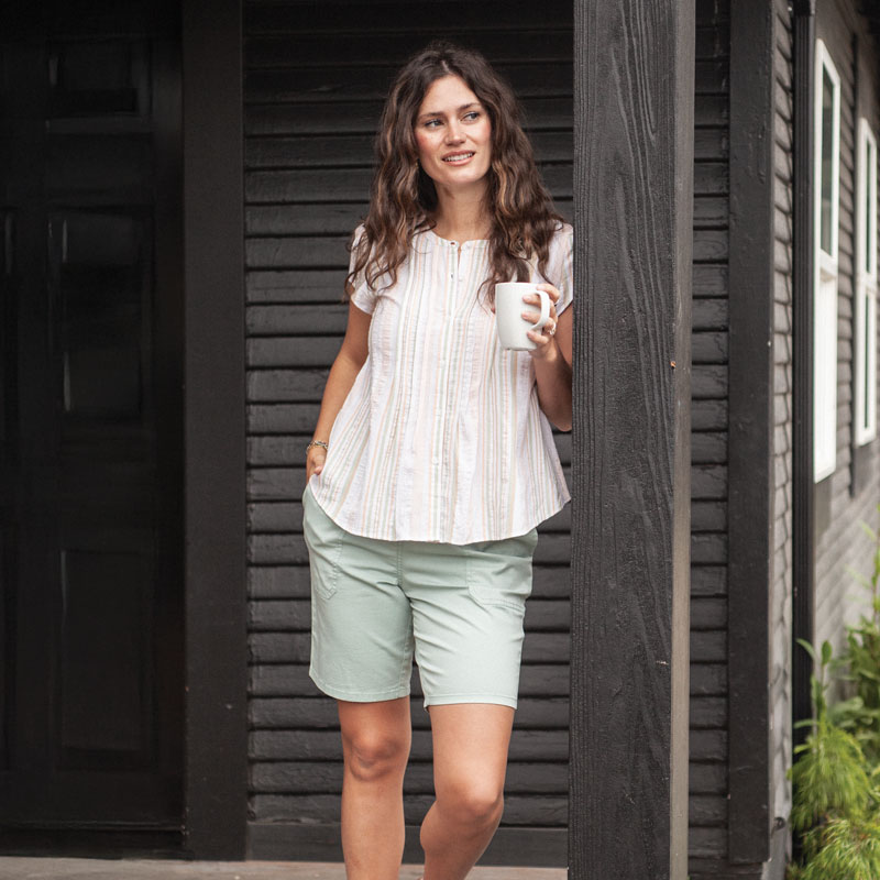 Woman standing on porch with coffee cup in hand.